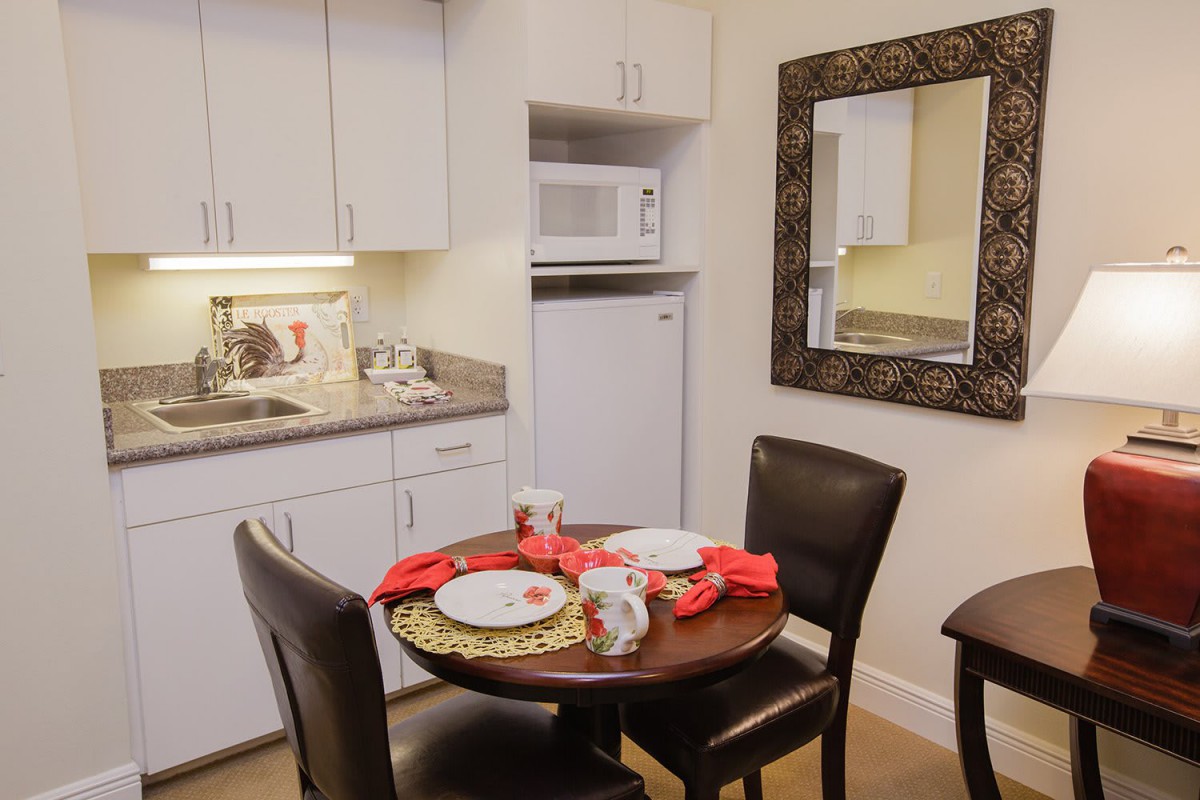 A cozy dining area with a set table next to a compact kitchen, featuring a microwave and refrigerator.