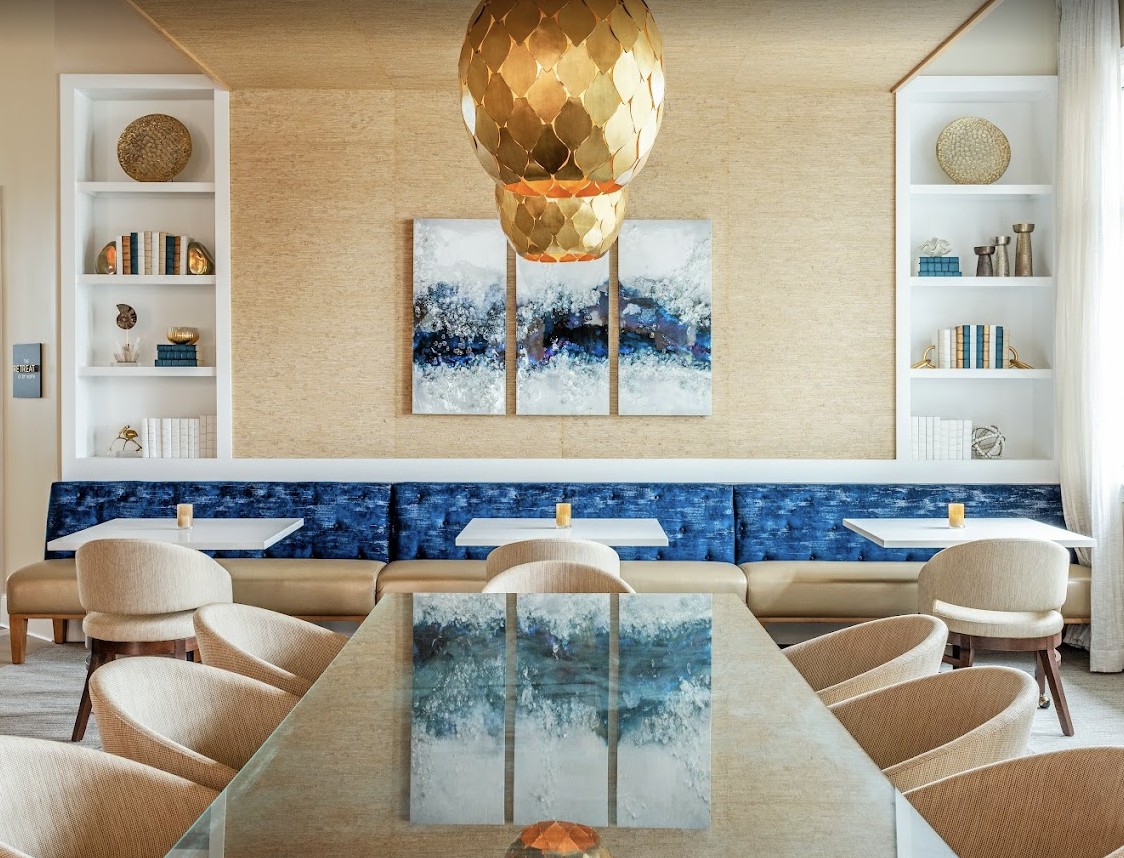 A modern and elegant dining area featuring a large pendant light, contemporary artwork, and plush seating.