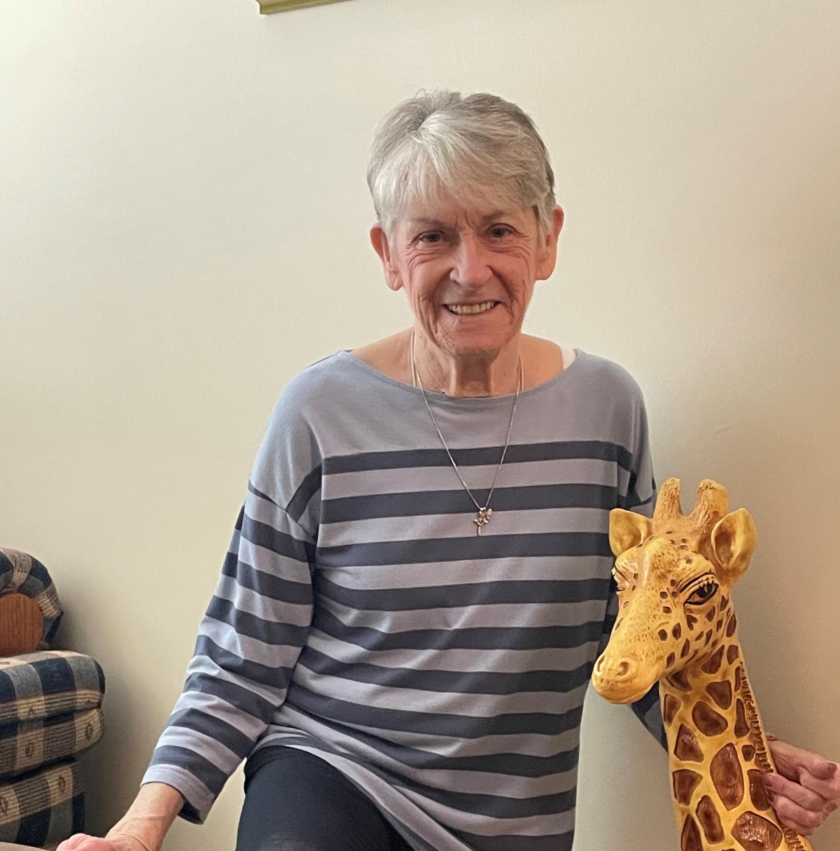A smiling woman in a striped shirt poses indoors with a stuffed giraffe.