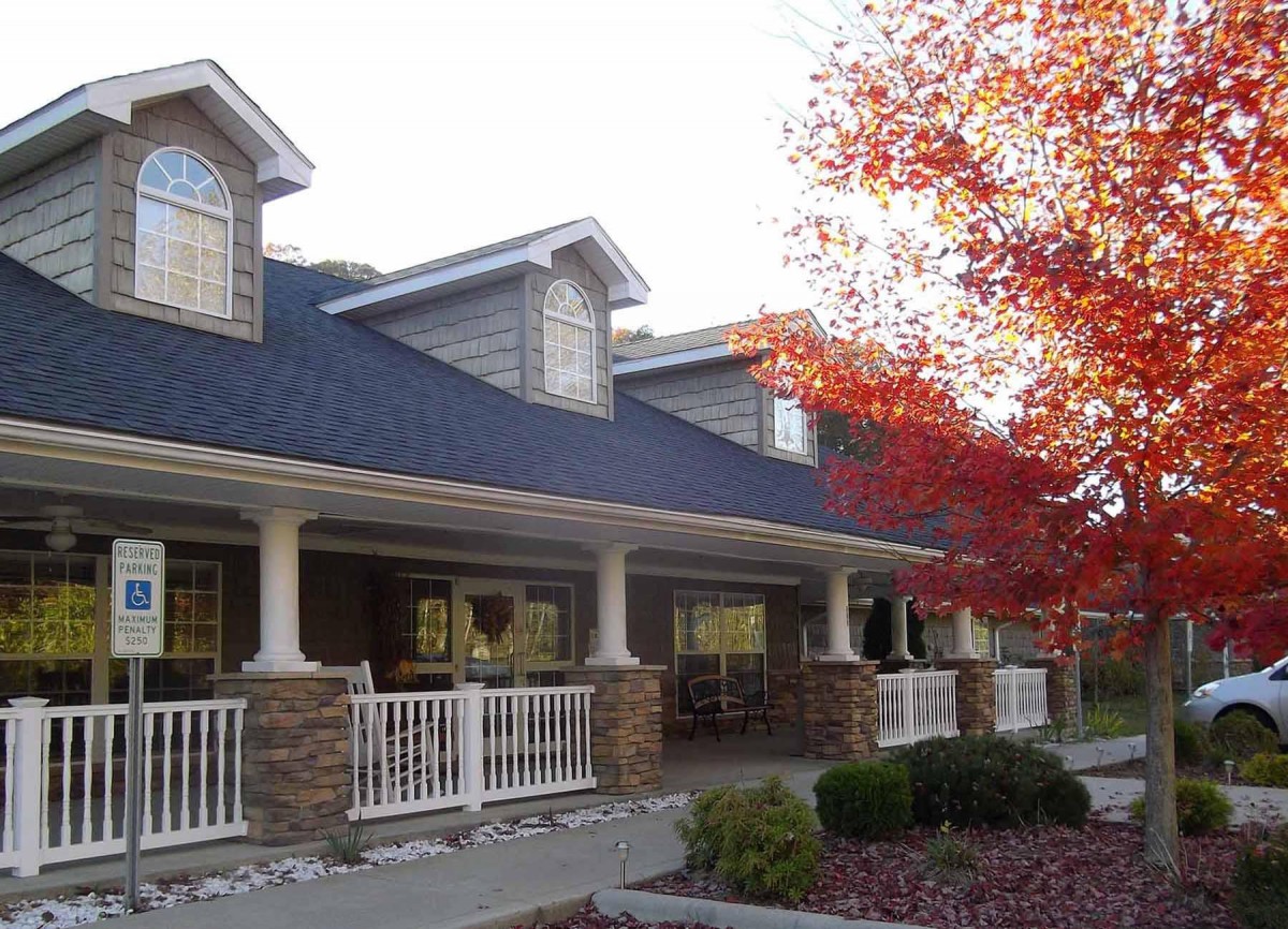 A building with a porch surrounded by autumn foliage and red-leafed trees.