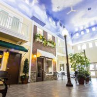 A spacious indoor atrium with a sky-themed ceiling, streetlamps, and lush greenery.