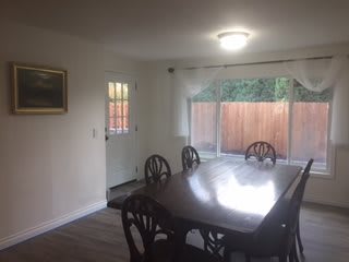 A dining room with a wooden table and chairs, featuring a window and door.