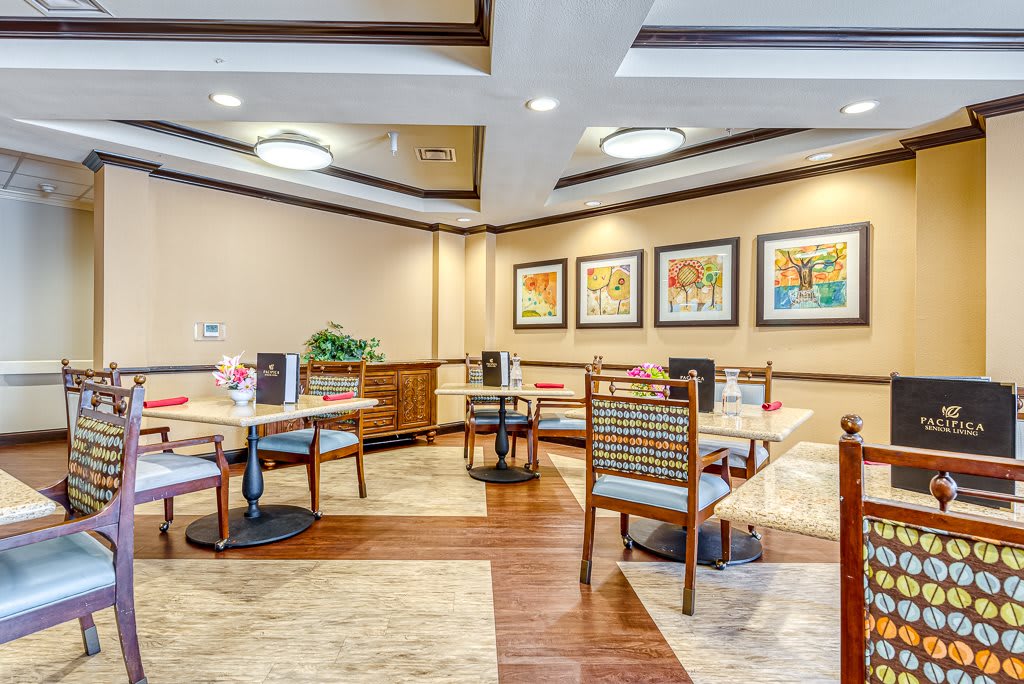 A cozy dining area with neatly arranged tables and chairs, featuring wall art and modern lighting.