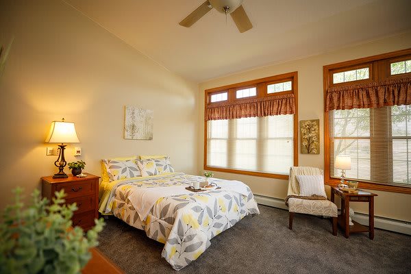 A cozy bedroom with a floral bedspread, warm lighting, and large windows.