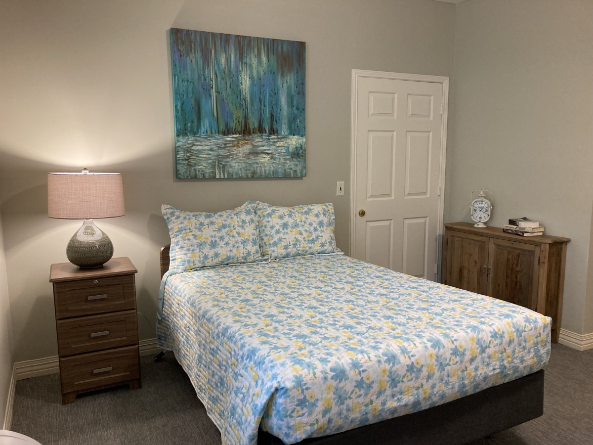 A cozy bedroom with a bed featuring patterned bedding, a bedside lamp, and artwork on the wall.