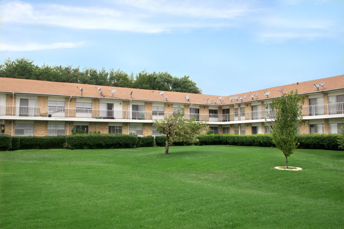 A residential building surrounded by a well-maintained green lawn and trees under a clear blue sky.