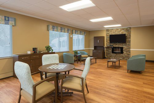 A cozy living room area with modern furniture, including a round table, chairs, and a television mounted above a fireplace.