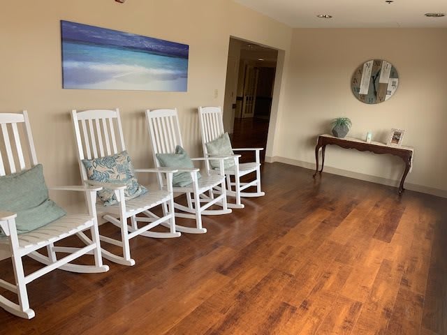 A cozy lobby with white rocking chairs and a wooden floor.