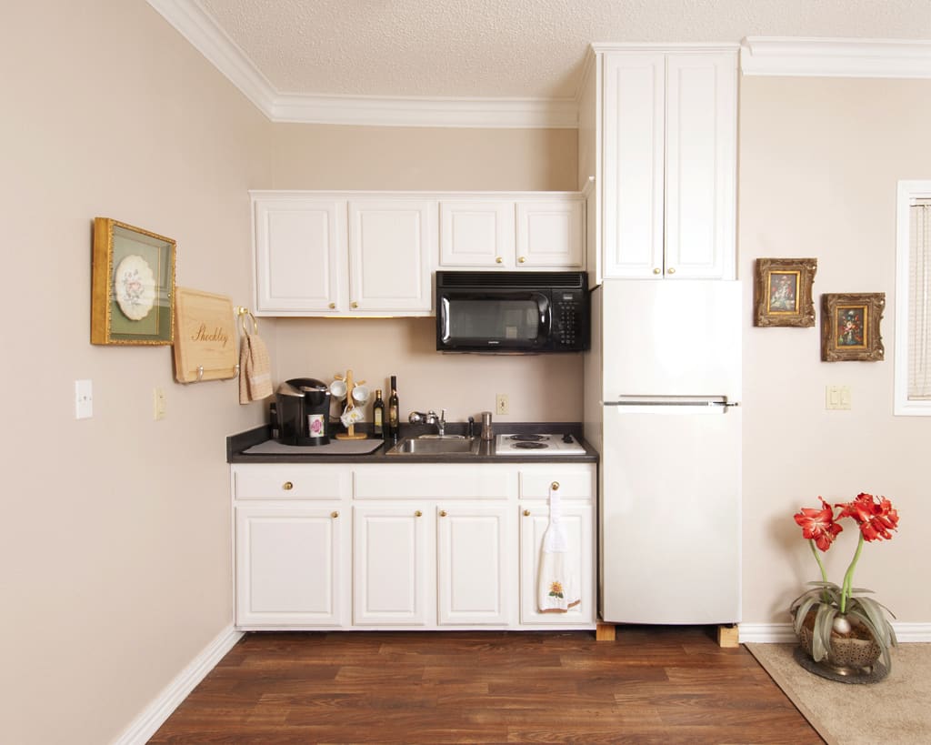 A compact kitchen featuring white cabinets, a refrigerator, microwave, and stove.