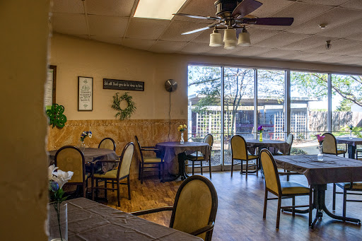 A cozy dining area with natural light streaming through large windows, featuring elegant chairs and tables.