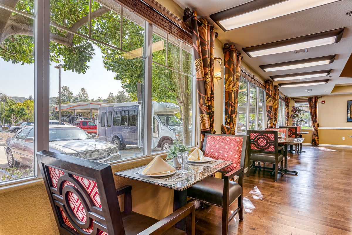 A cozy restaurant interior with elegantly set tables and large windows offering a street view.