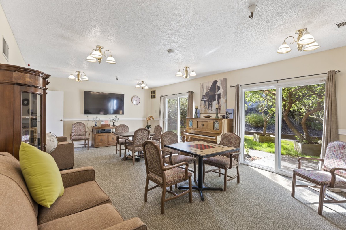 Spacious living room with comfortable seating, a television, and a piano, illuminated by natural light from large windows.