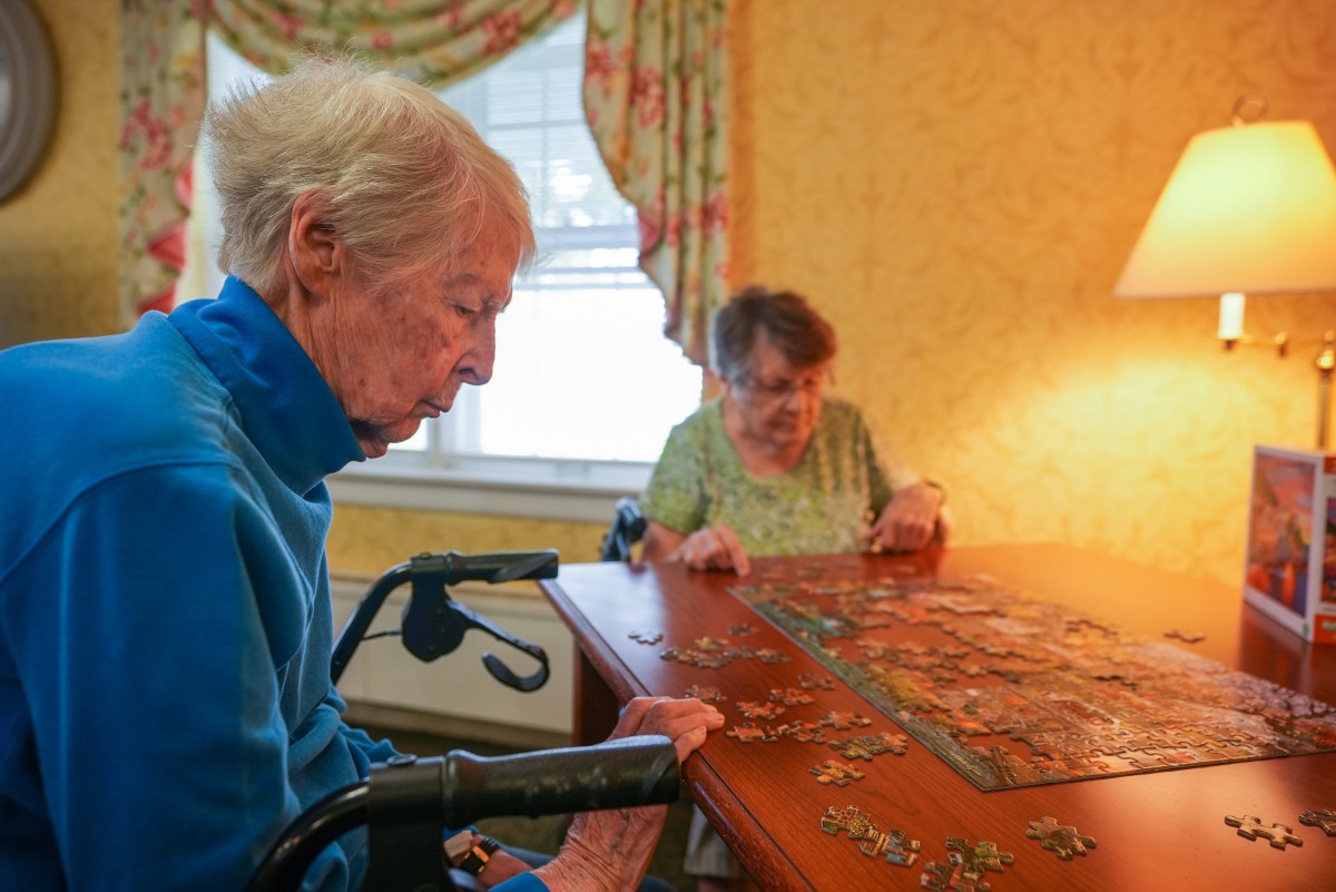 Two elderly individuals working on a puzzle together at a table in a cozy room.