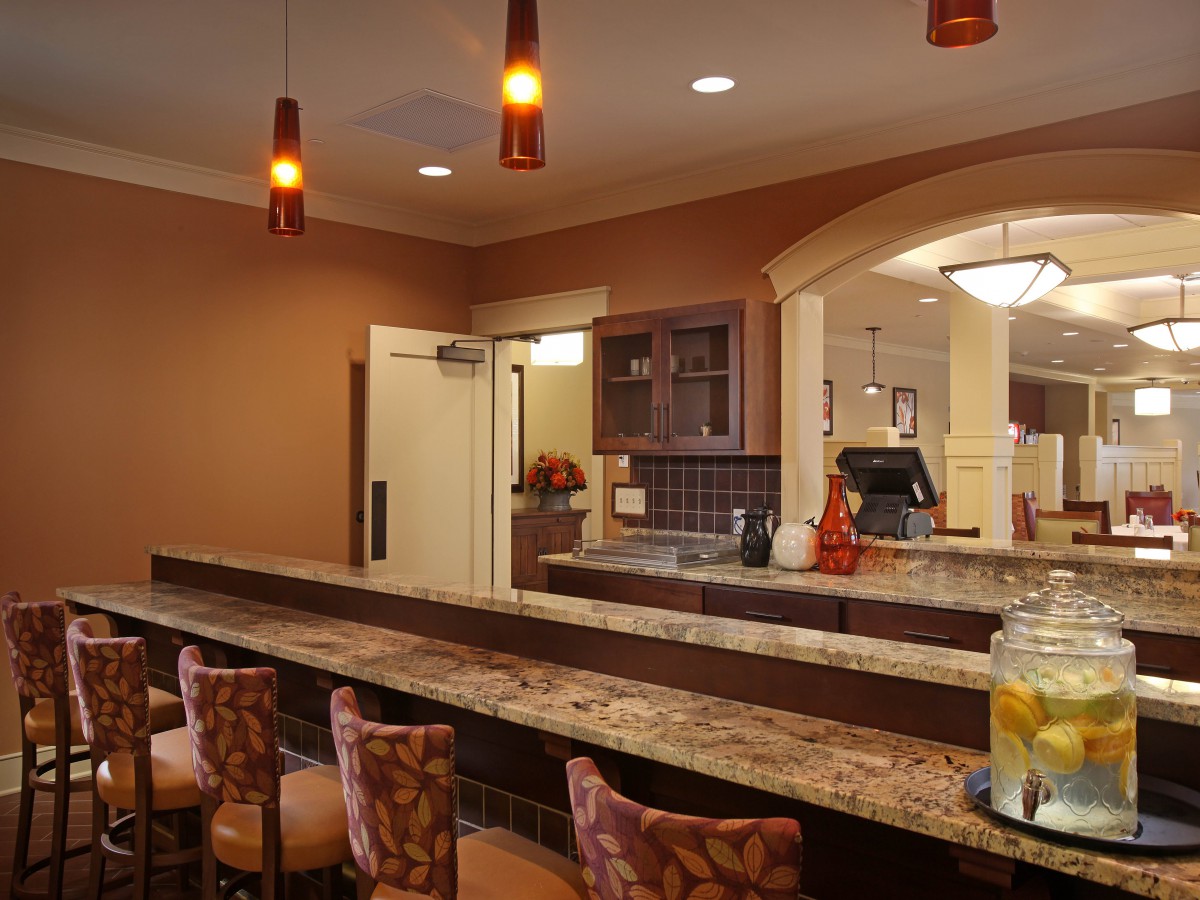 A modern kitchen with a long counter and cozy seating, illuminated by stylish pendant lights.