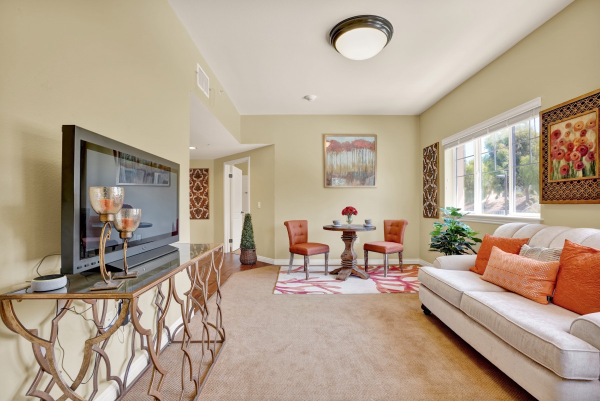 A cozy living room with a dining area, featuring a sofa, small dining table with chairs, and plenty of natural light through a large window.