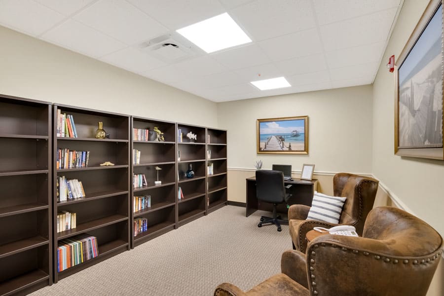 A cozy office library with bookshelves, a computer desk, and comfortable armchairs.