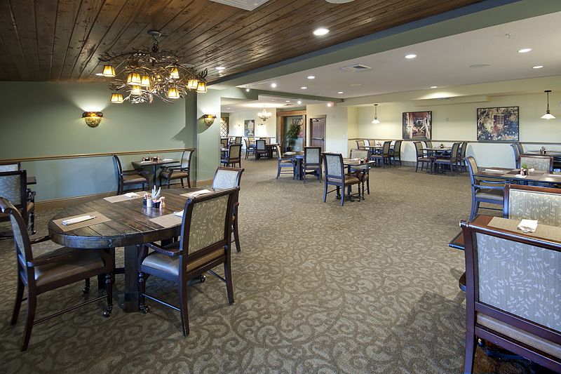 An empty restaurant dining area with neatly arranged tables and chairs, featuring a chandelier and carpeted flooring.