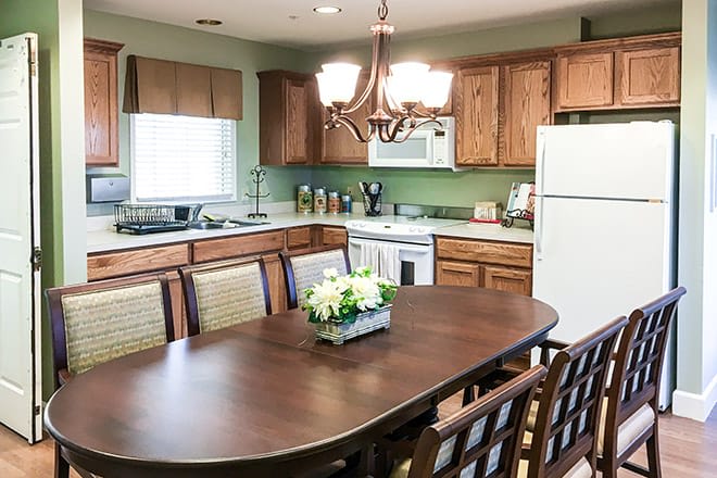 A cozy kitchen with a wooden dining table and matching chairs, featuring warm cabinets, a chandelier above, and essential appliances.