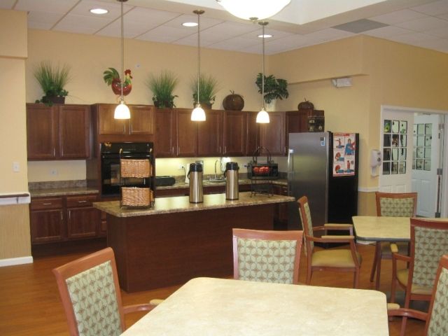 A modern kitchen interior with wooden cabinets, an island, chairs, and pendant lighting.