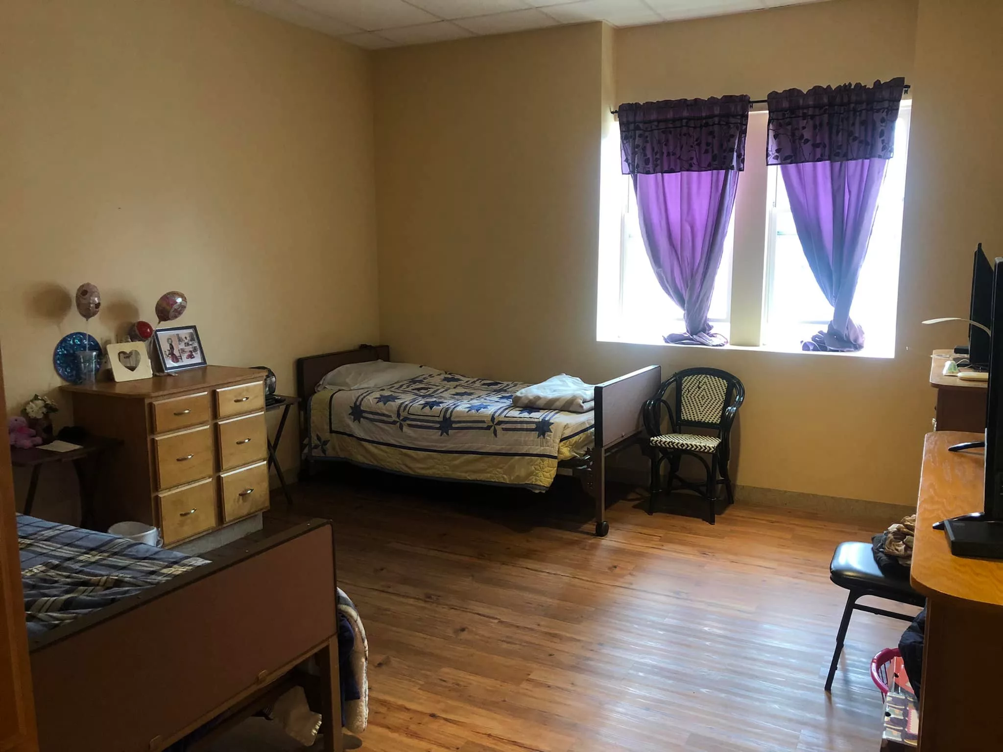 A cozy bedroom with a single bed and purple curtains on the windows.