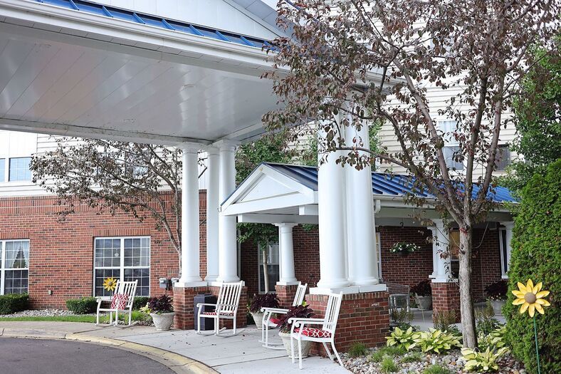 A building entrance with large columns, benches, and surrounding trees.