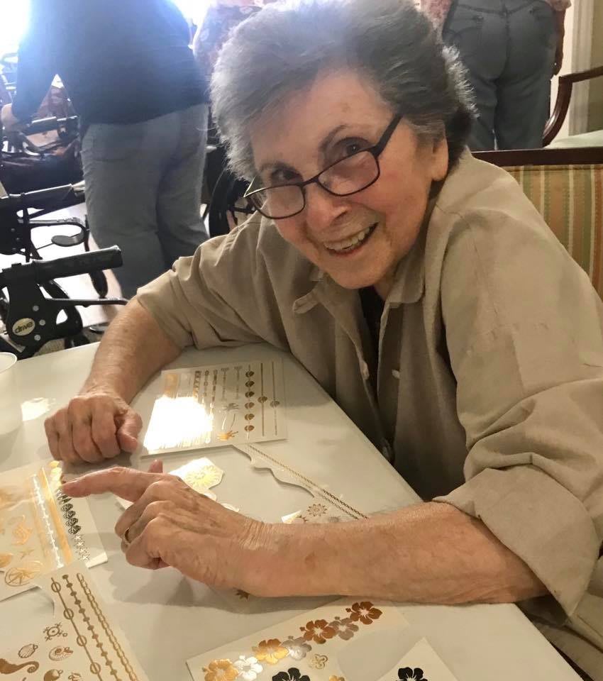 An elderly woman smiling while seated at a table indoors.