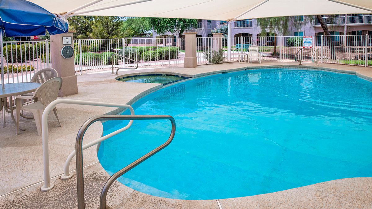 A serene outdoor swimming pool with a safety fence and shade umbrellas.
