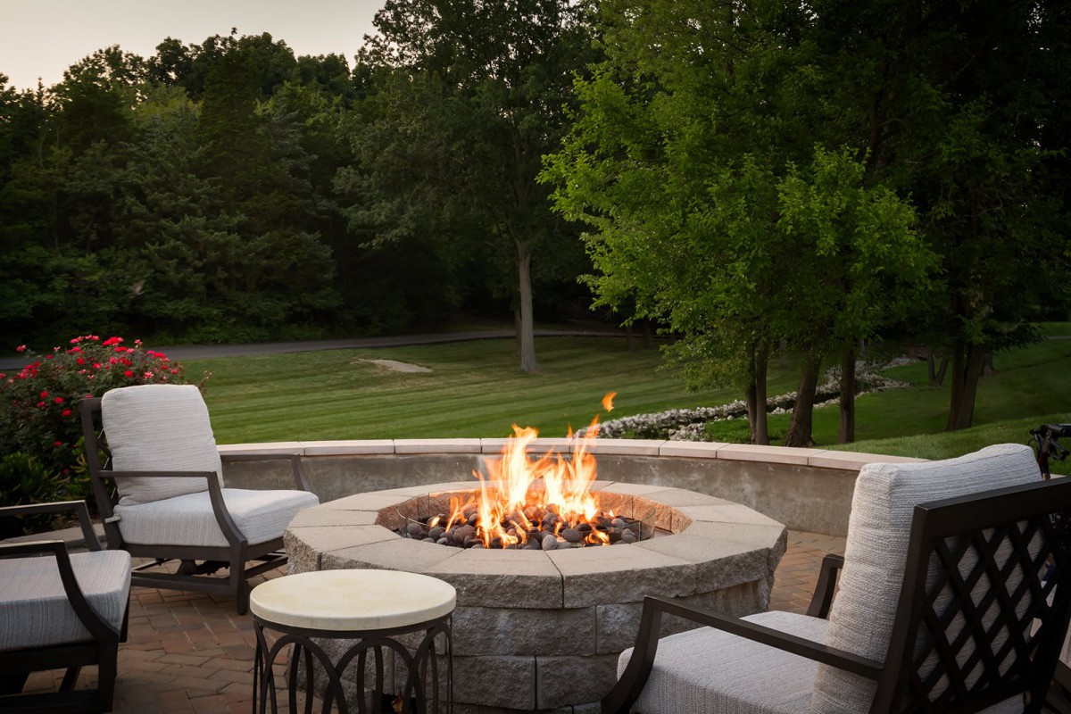 A cozy outdoor setting featuring a fire pit surrounded by comfortable seating, overlooking a lush garden.