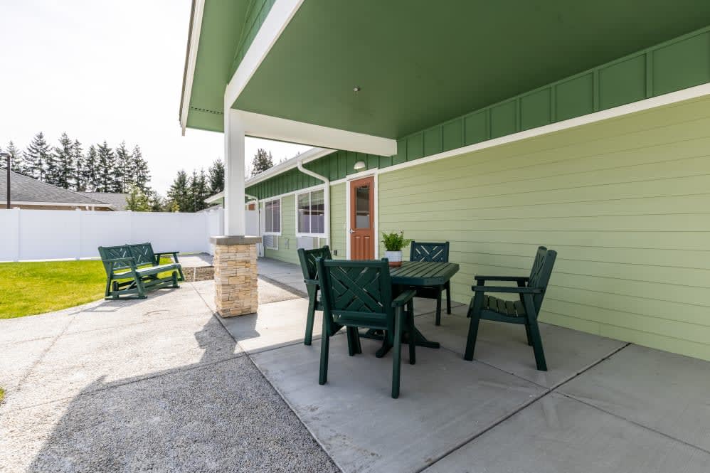 A cozy backyard patio with a set of green outdoor chairs and a table under a covered area.
