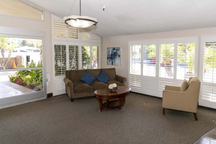 A cozy living room with a sofa, armchair, coffee table, and large windows with shutters.