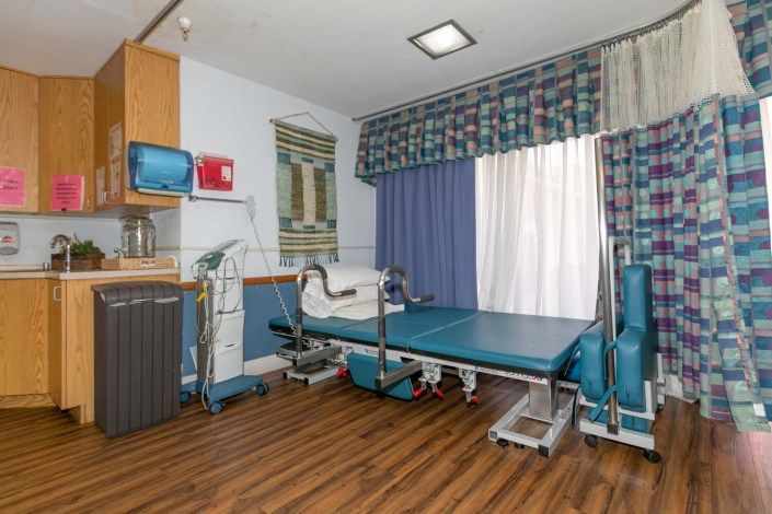 A hospital room equipped with medical devices and a bed, featuring patterned curtains and wooden flooring.