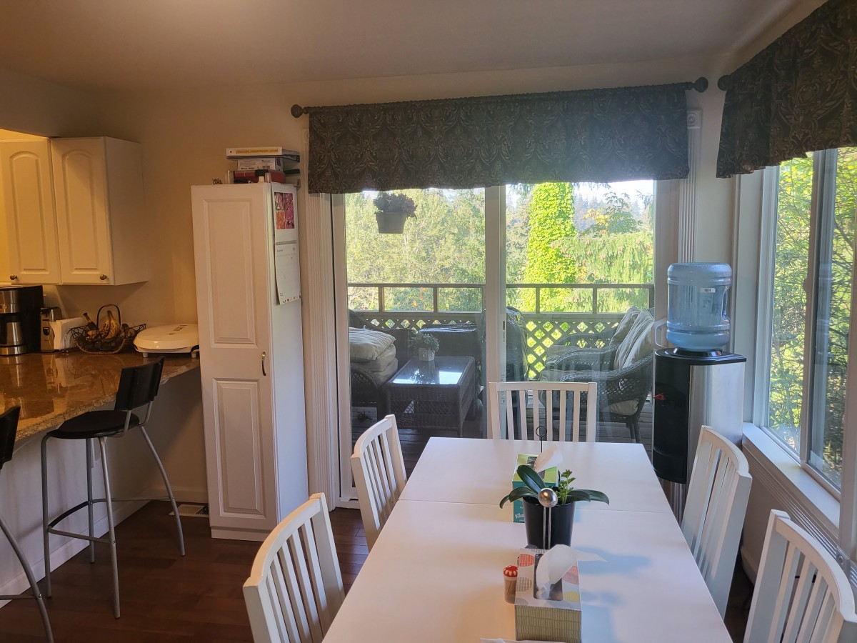 A bright dining area with a white table and chairs, featuring an indoor plant and a view through sliding glass doors.