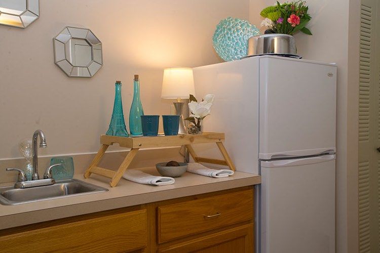 A well-decorated kitchen counter with teal bottles, a small lamp, and flowers next to a refrigerator.