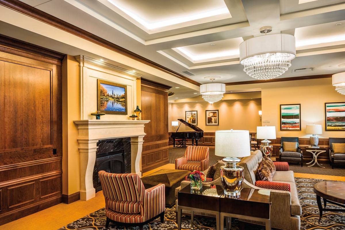 A luxurious lobby interior featuring elegant furniture, a fireplace, and a grand piano under ornate chandeliers.