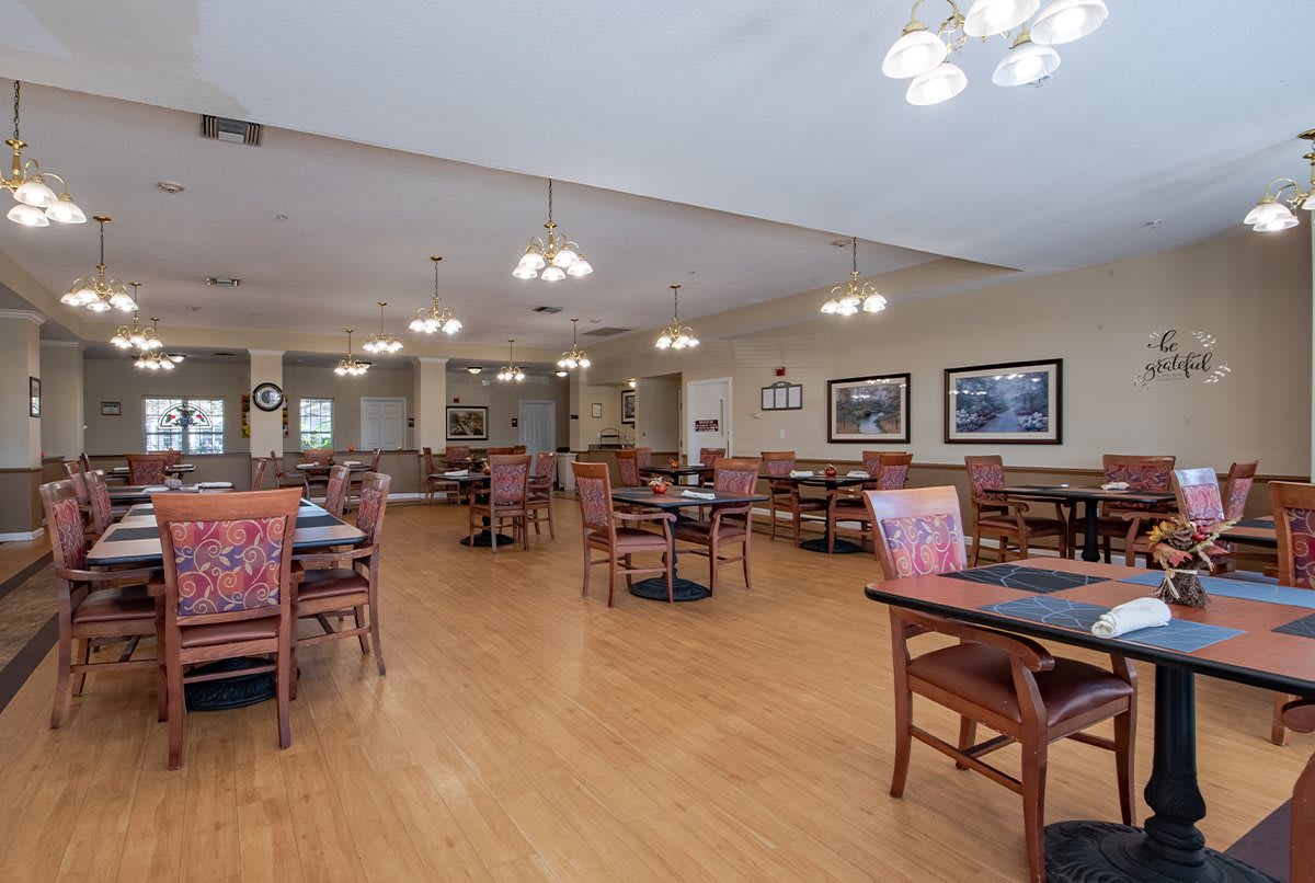 An empty dining room with neatly arranged tables and chairs, featuring warm lighting and wooden flooring.