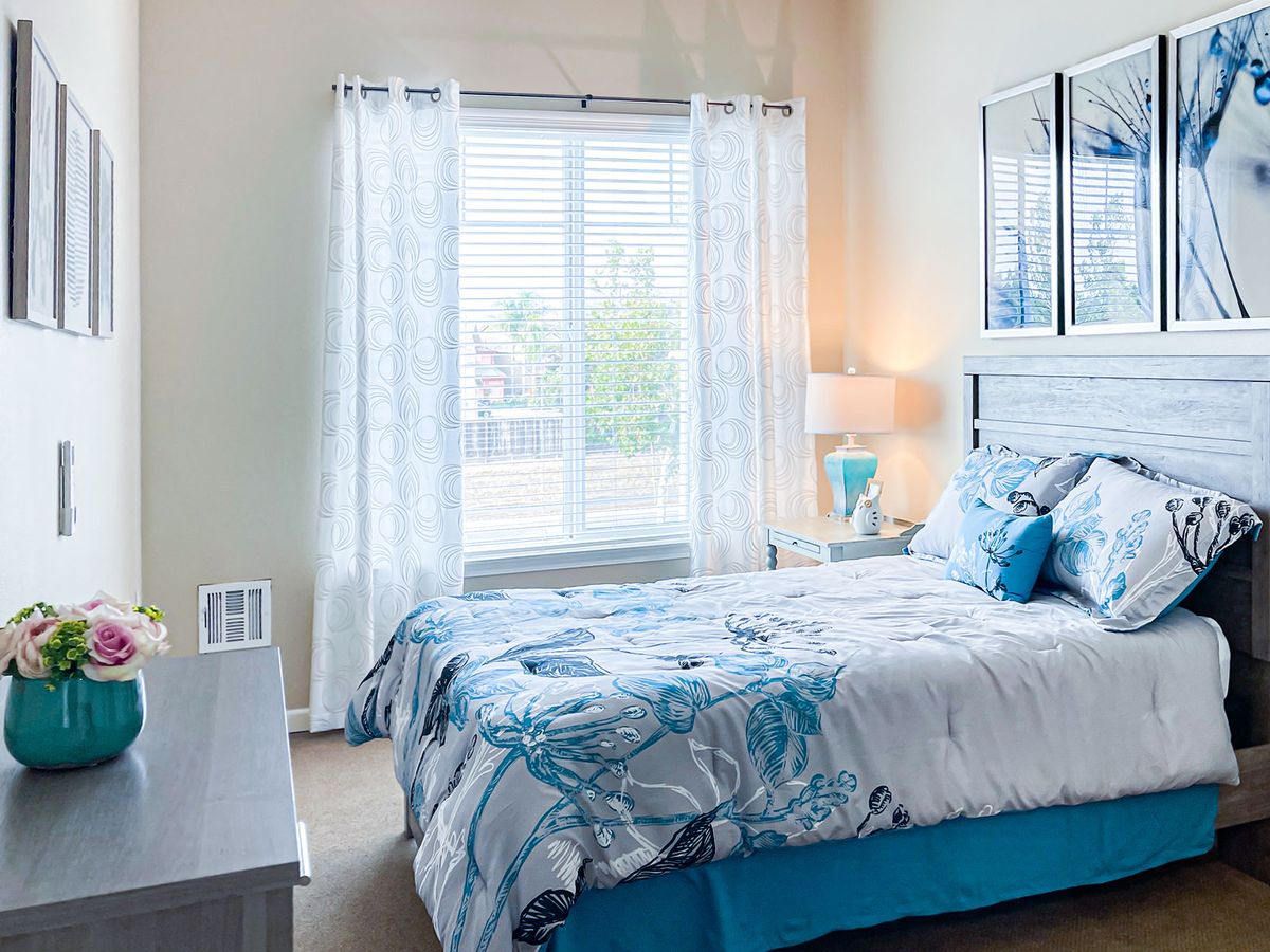 A cozy bedroom with blue and white decor, featuring a bed by the window with sheer curtains.