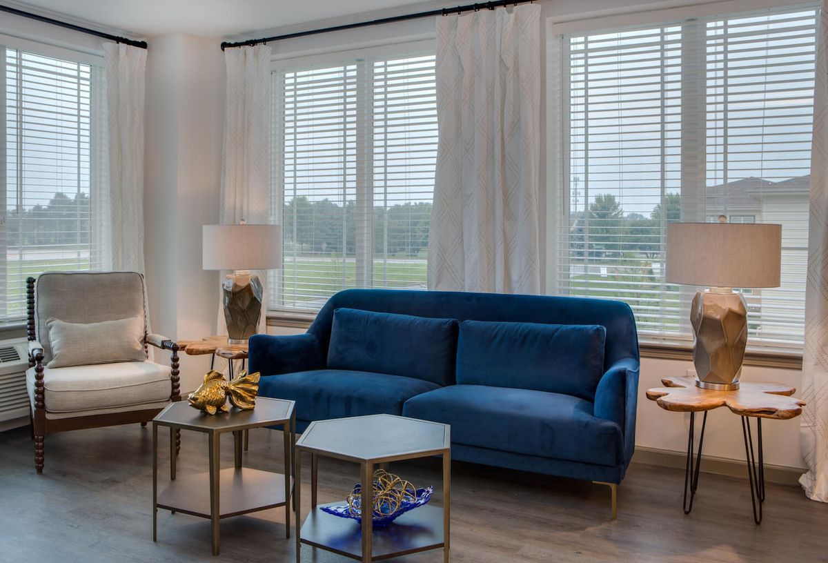 A modern living room with a blue sofa, decorative tables, and large windows.