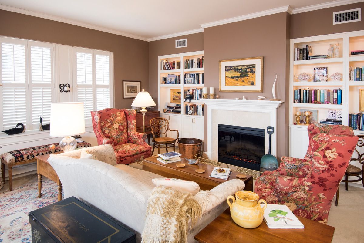 A cozy living room featuring a fireplace, bookshelves, and a mix of armchairs and sofa for seating.
