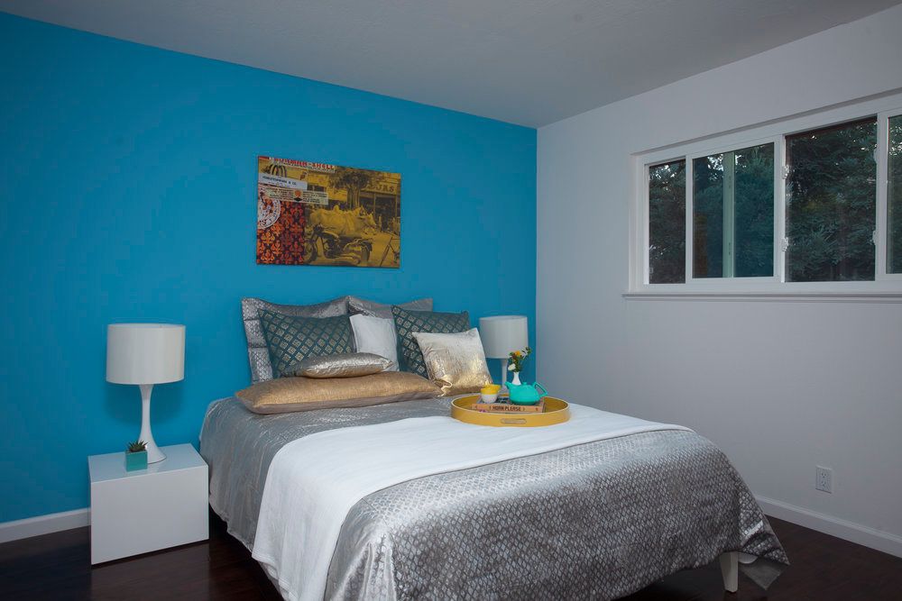 A modern bedroom with a blue accent wall and decorative pillows.