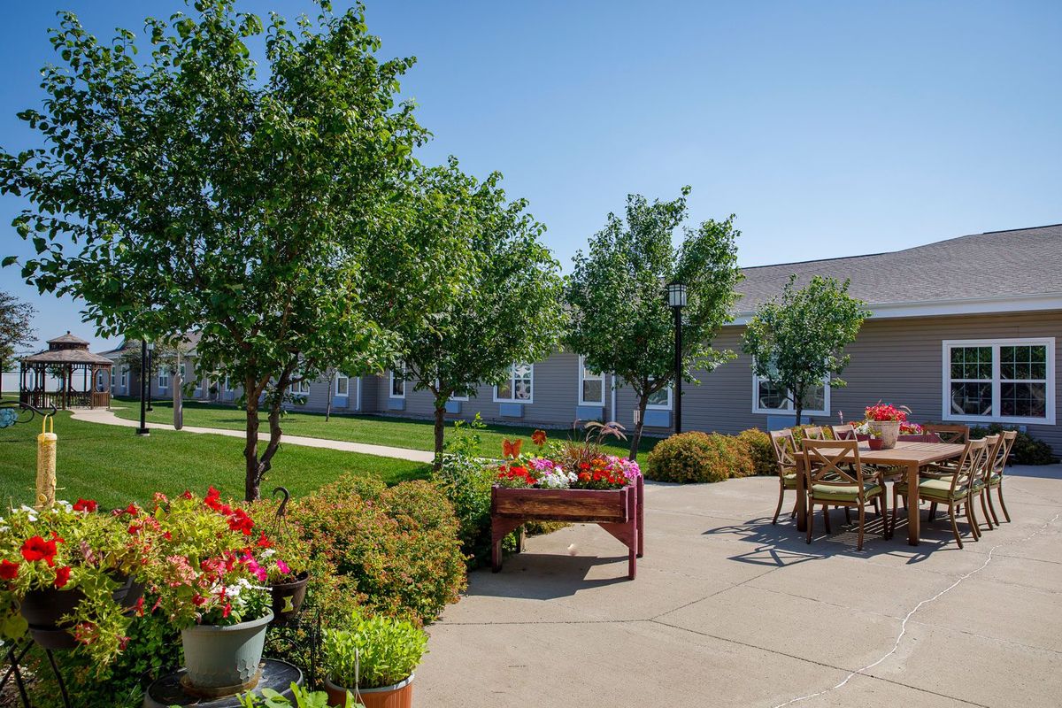 A sunny outdoor patio with tables and chairs surrounded by trees and vibrant flowers.