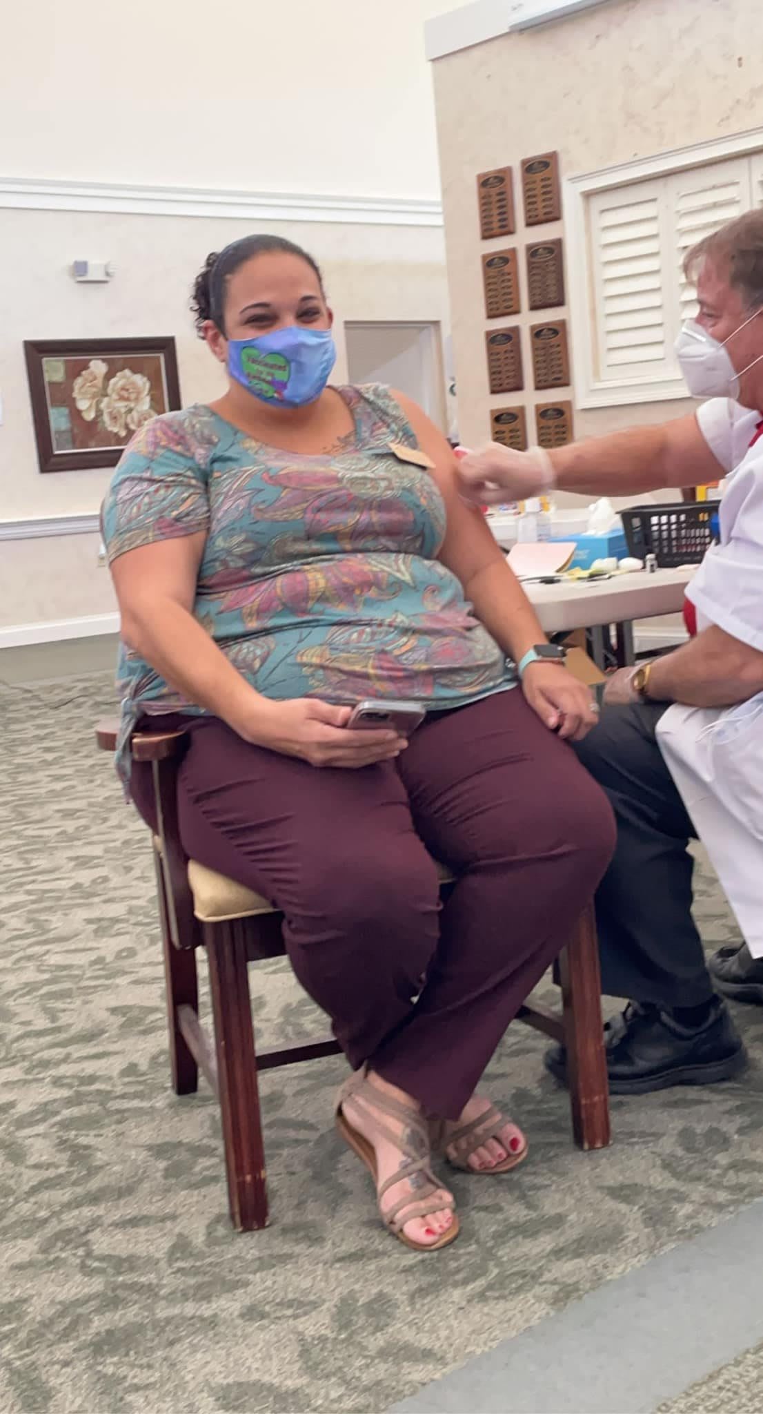 A healthcare worker administering a vaccine to a seated individual wearing a mask.