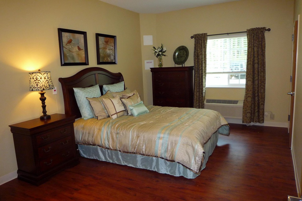 A cozy bedroom with a neatly made bed, artwork on the walls, and wooden flooring.