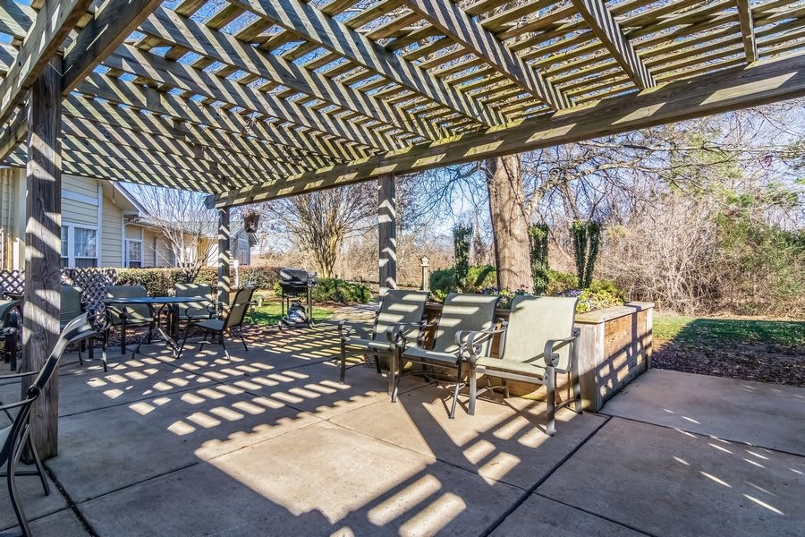 A sunlit patio with a pergola casting intricate shadows over outdoor furniture.