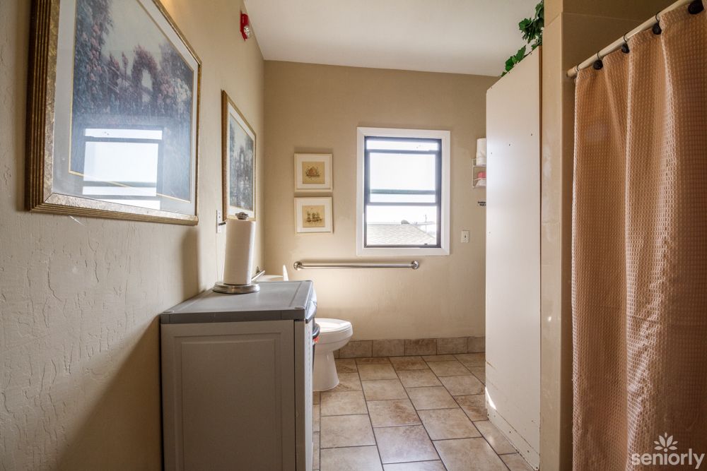 A well-lit bathroom with a tiled floor, featuring a toilet, sink, and decorative wall art.