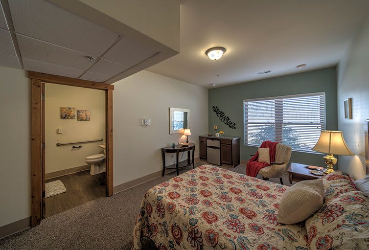 A cozy bedroom with floral bedding, a chair, and a large window allowing natural light to enter.