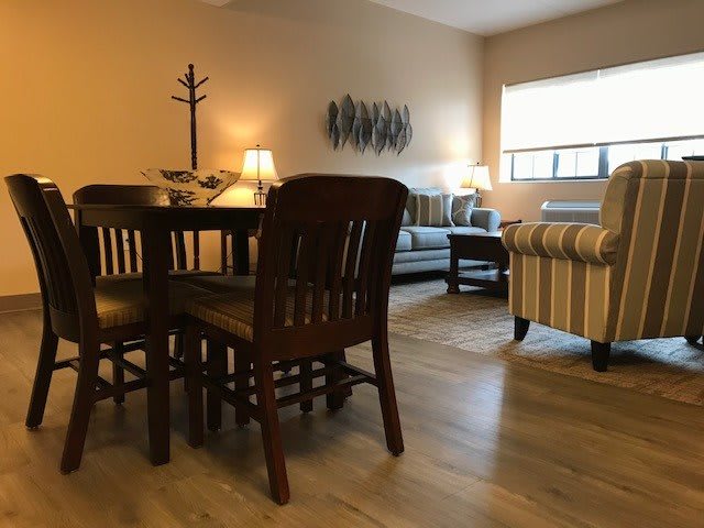 A cozy living room featuring a dining area with a wooden table and chairs, a sofa, and elegant lighting.
