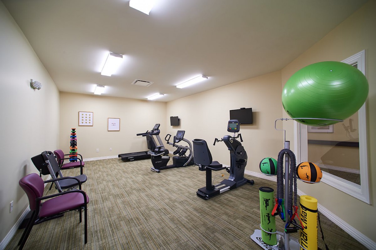 A small gym with exercise equipment including treadmills, stationary bikes, and exercise balls.