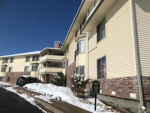 A multi-story apartment building with snow on the ground, set against a clear blue sky.