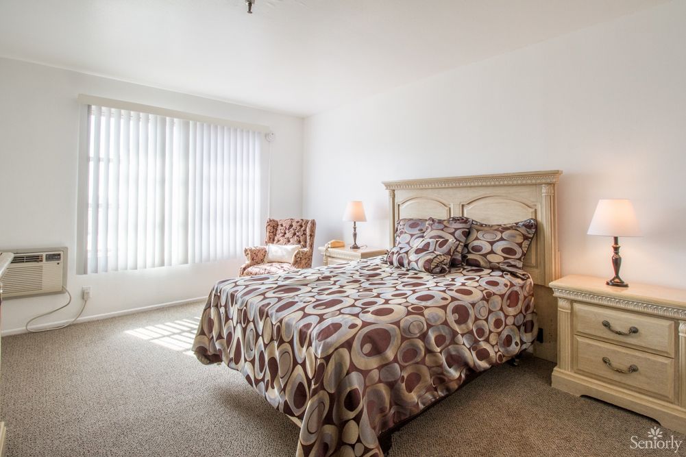 A cozy bedroom with a patterned bedspread, armchair, and soft lighting from a lamp by the window.