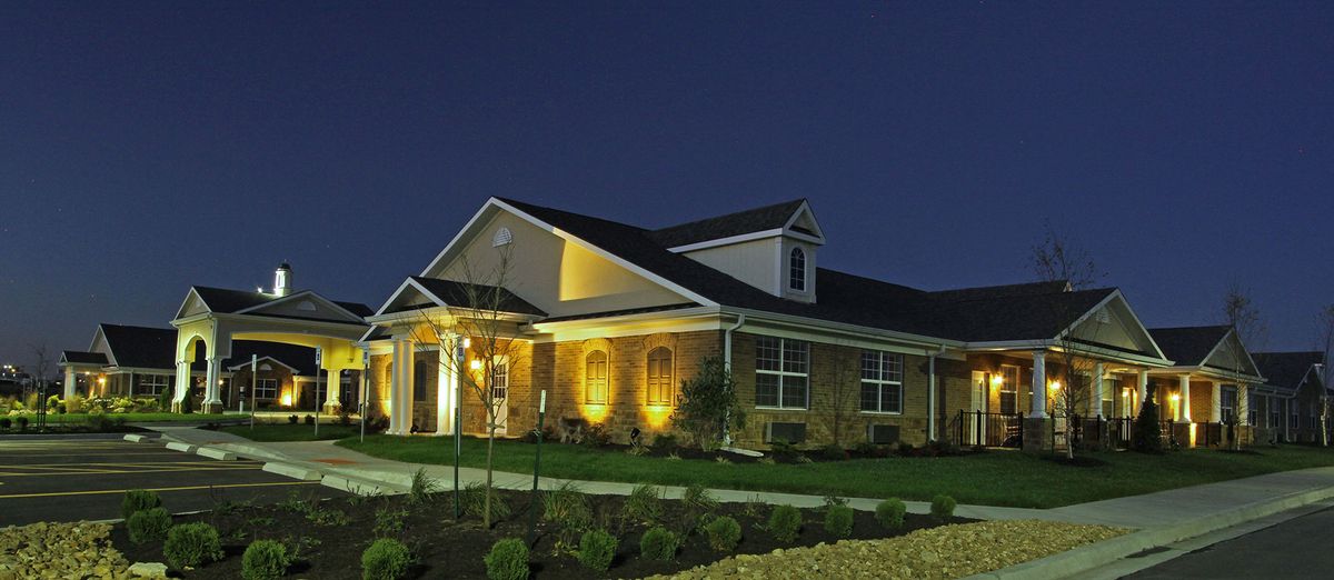 A well-lit suburban house at night with a brick exterior and landscaped front yard.